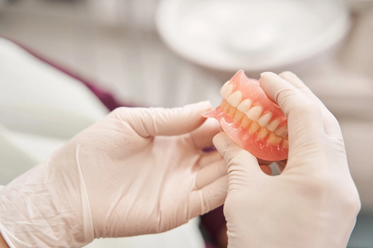 Gloved hands holding a full set of dentures